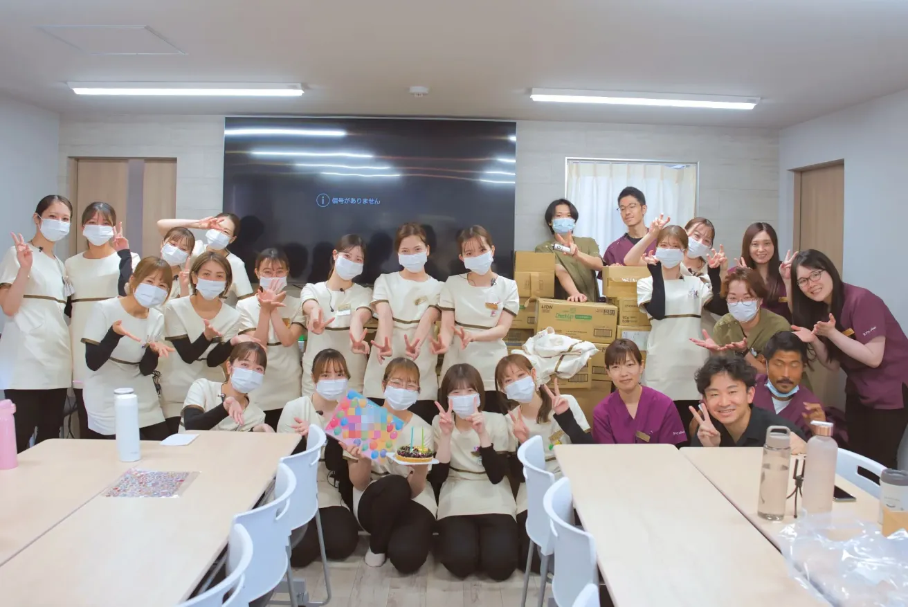 会議室で、ピースをしたりしゃがんだりして並ぶ大勢のスタッフ