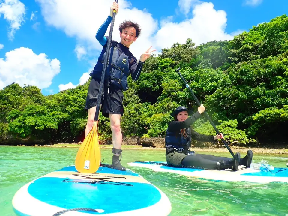 海でSUP（立って漕ぐボード）に乗り、ピースをする院長