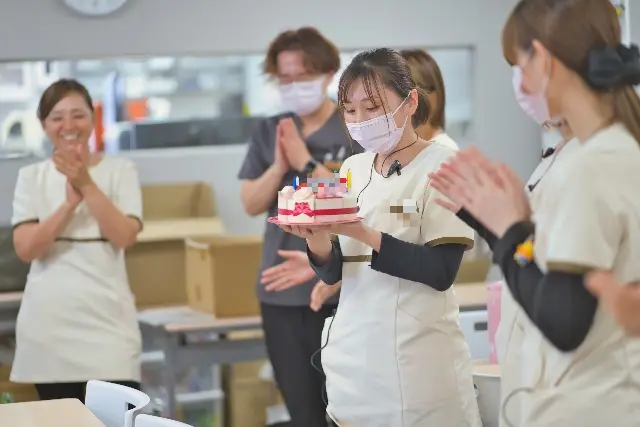 ケーキを持ったスタッフを、みんなが拍手でお祝いしている